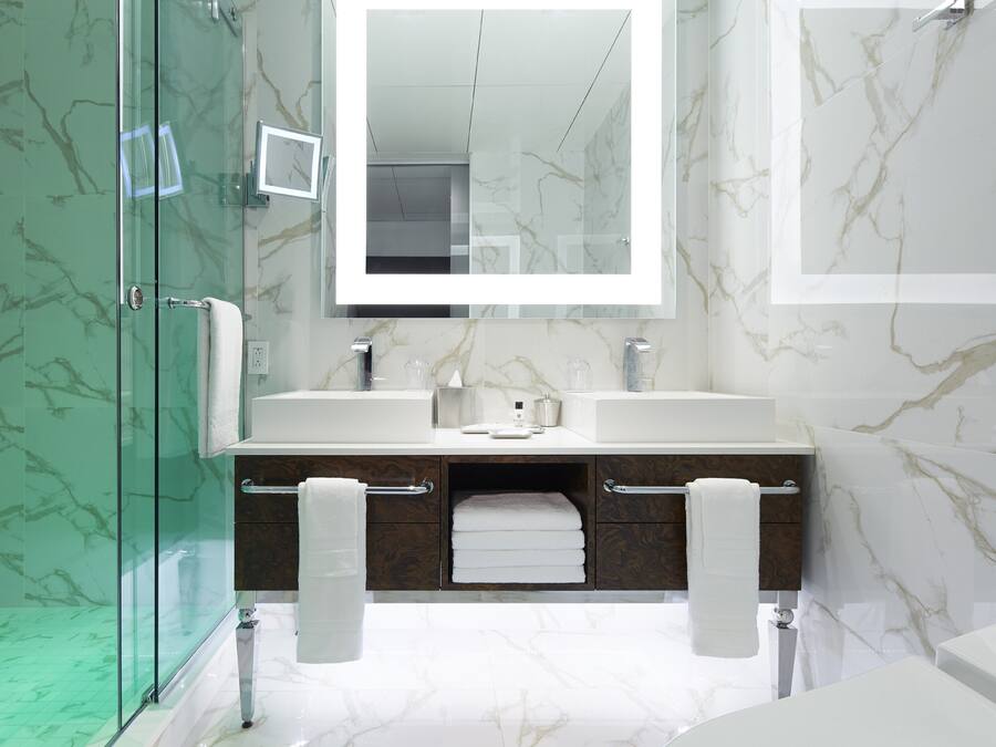 Un baño moderno con cabina de ducha de vidrio, pared con azulejos de mármol, espejo grande y tocador doble.