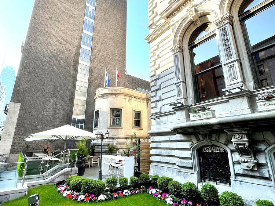 A courtyard with a modern building, a classical building, and a small garden area with steps and outdoor seating.