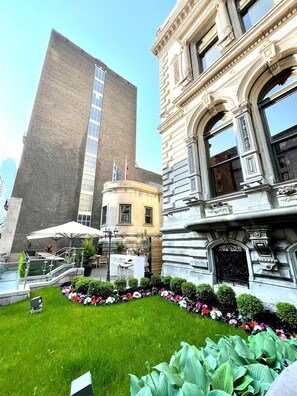 A courtyard with a modern building, a classical building, and a small garden area with steps and outdoor seating.