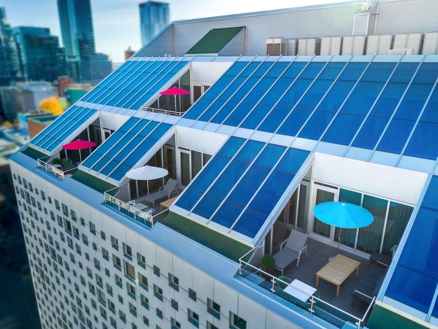 A modern building with a rooftop terrace featuring solar panels, outdoor seating, and large windows.
