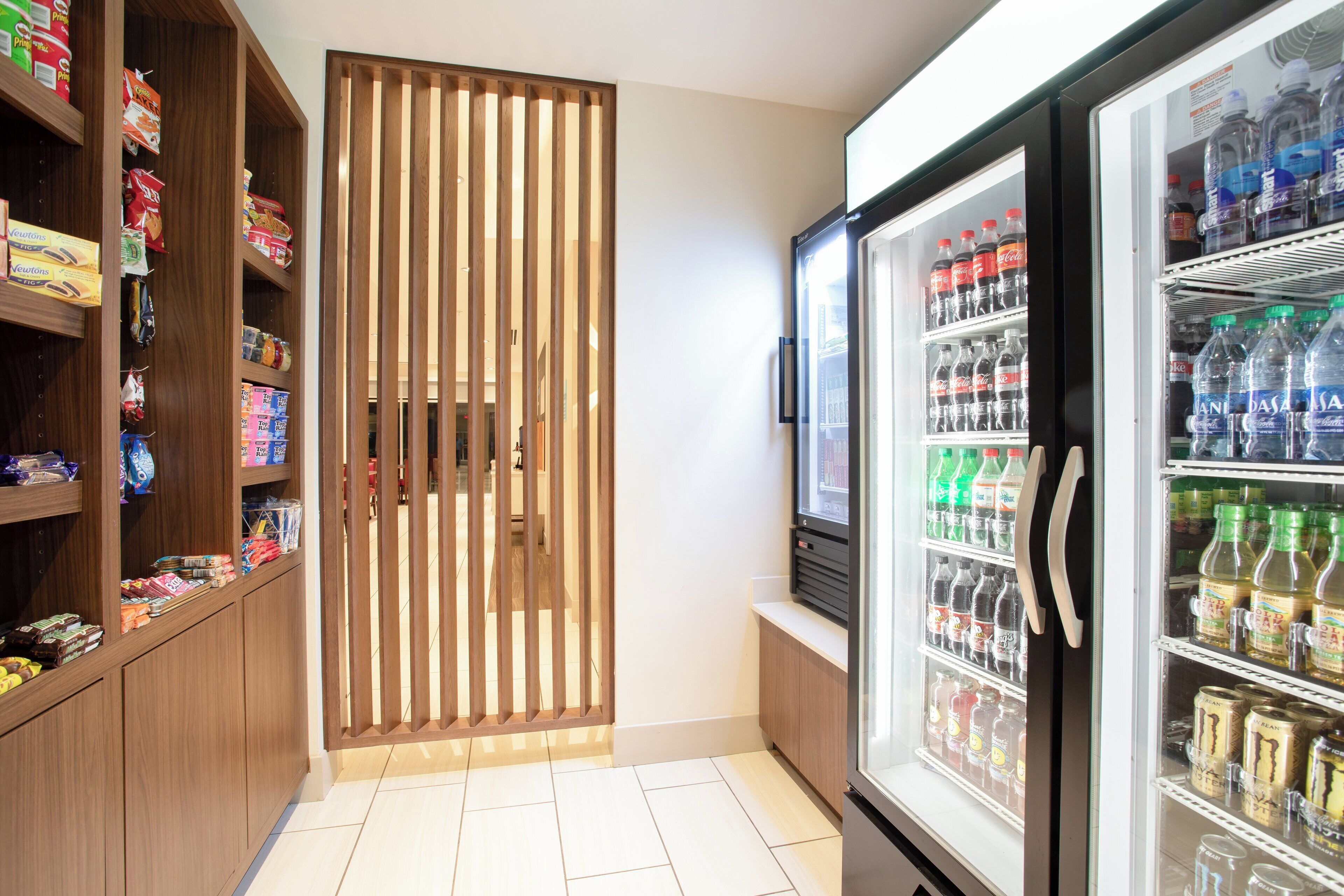 Una habitación pequeña con un refrigerador lleno de bebidas, un mueble de madera con aperitivos y una puerta corredera.