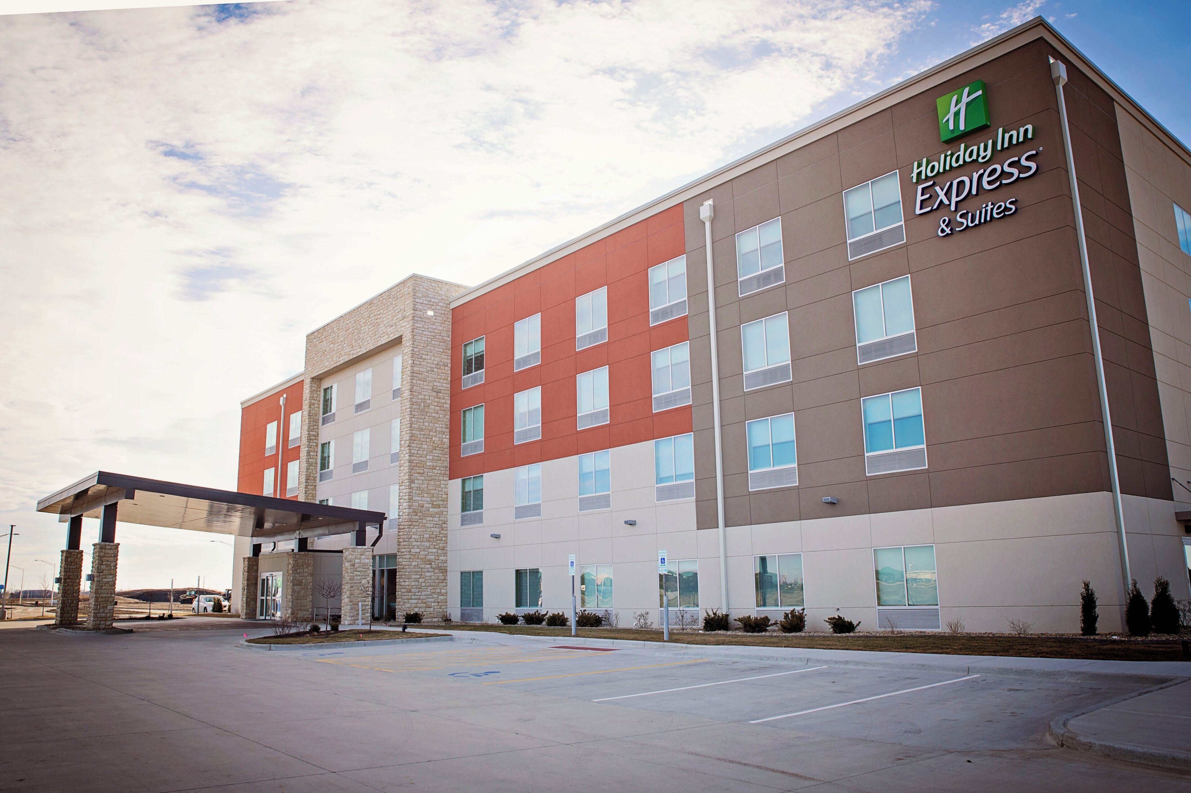 A Holiday Inn Express & Suites hotel with a modern design, featuring a mix of brick and stucco exterior, multiple windows, and a covered parking area.