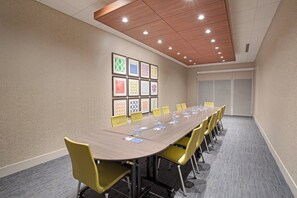 A conference room with a long table, yellow chairs, and framed artwork on the wall.