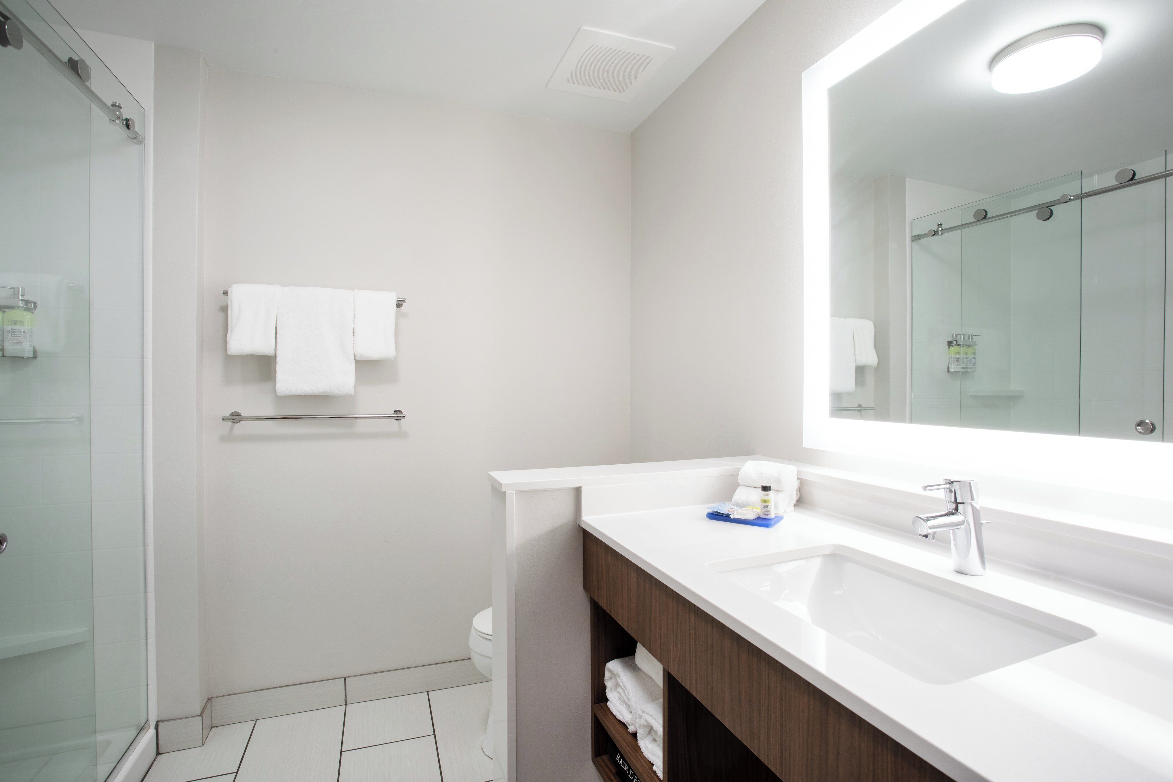 A modern bathroom with a glass shower enclosure, a white sink with a mirror, and a towel rack.