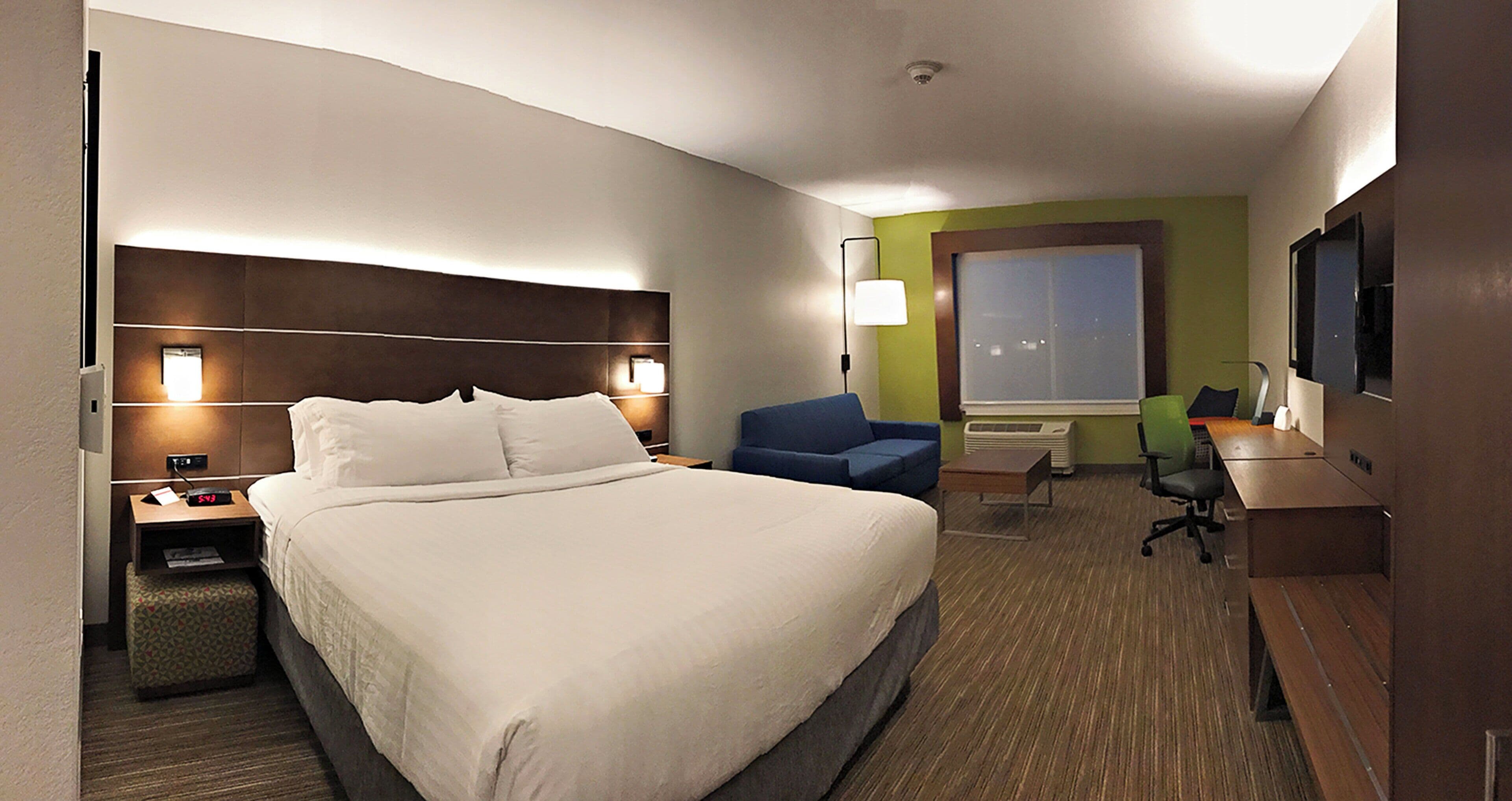 A hotel room with a large bed, a desk with a chair, a small table, a sofa, and a television.