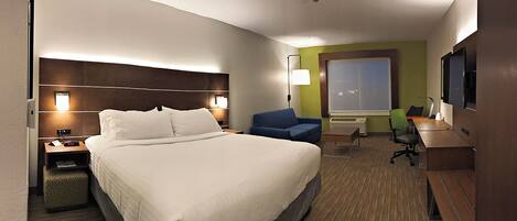A hotel room with a large bed, a desk with a chair, a small table, a sofa, and a television.