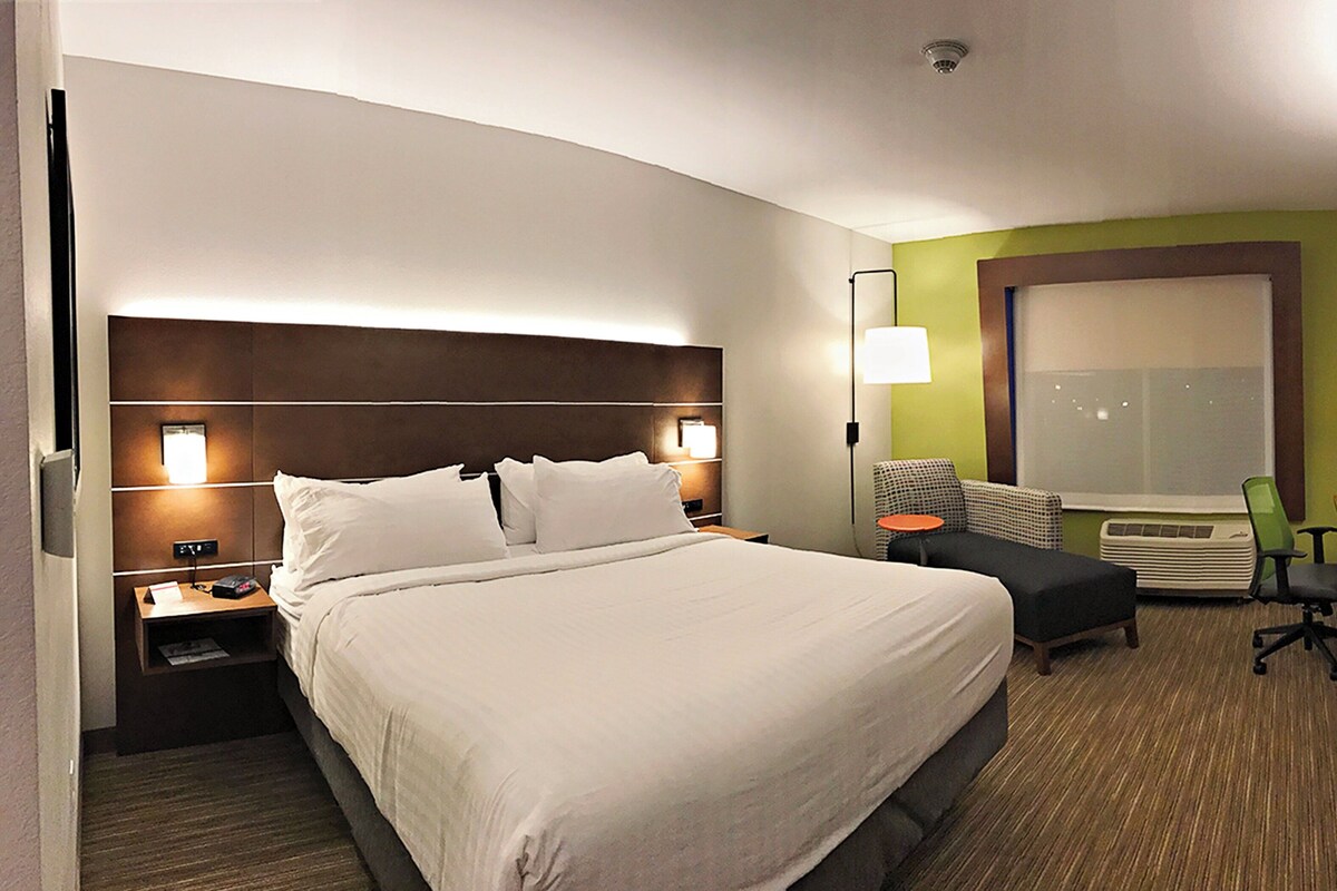 A hotel room with a large bed, bedside tables, a desk, a chair, a television, and a window.