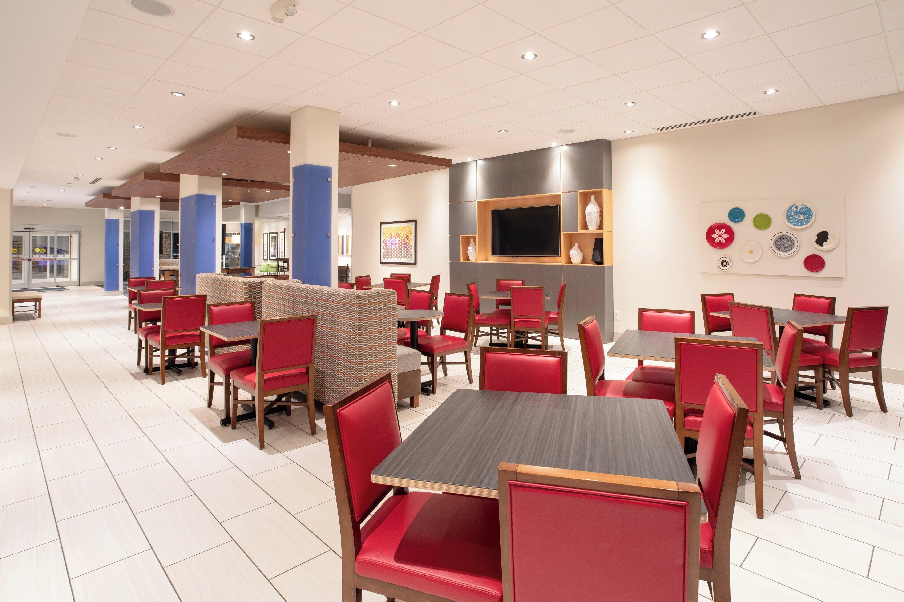 A modern restaurant with red upholstered chairs and tables, a flat-screen TV mounted on the wall, and a variety of decorative plates on display.