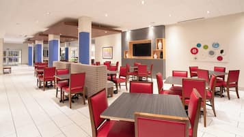 A modern restaurant with red upholstered chairs and tables, a flat-screen TV mounted on the wall, and a variety of decorative plates on display.