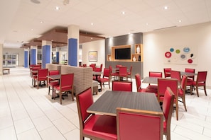 A modern restaurant with red upholstered chairs and tables, a flat-screen TV mounted on the wall, and a variety of decorative plates on display.