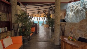 Eine Hotelhalle mit Steinwand, Holzbude und einer Sitzecke mit orangefarbenen Kissen.