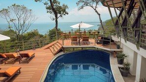 Ein Poolbereich mit Holzliegen und Blick auf das Meer.