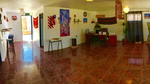 A spacious room with a tiled floor, a reception desk, a couch, and various decorations including flags and artwork. - Hostal Possada Atacameña (San Pedro de Atacama)