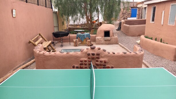 A ping pong table in a courtyard with a rustic, earthy-colored building in the background. - Hostal Possada Atacameña (San Pedro de Atacama)