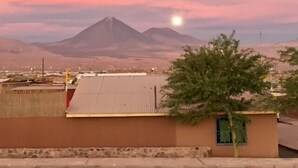 A building with a flat roof and a small window, set against a backdrop of mountains and a sunset sky. - Hostal Possada Atacameña (San Pedro de Atacama)