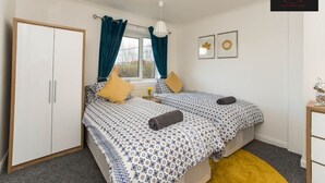 Une chambre à coucher avec un lit, une armoire, une fenêtre avec des rideaux, une table de chevet et un tableau au mur.