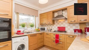 Une cuisine moderne avec des meubles en bois, un four encastré, un four à micro-ondes et une bouilloire rouge.
