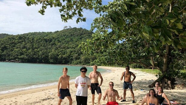 A group of people on a sandy beach with a forested hill in the background. - Hangover Hostel (Ko Phi Phi)