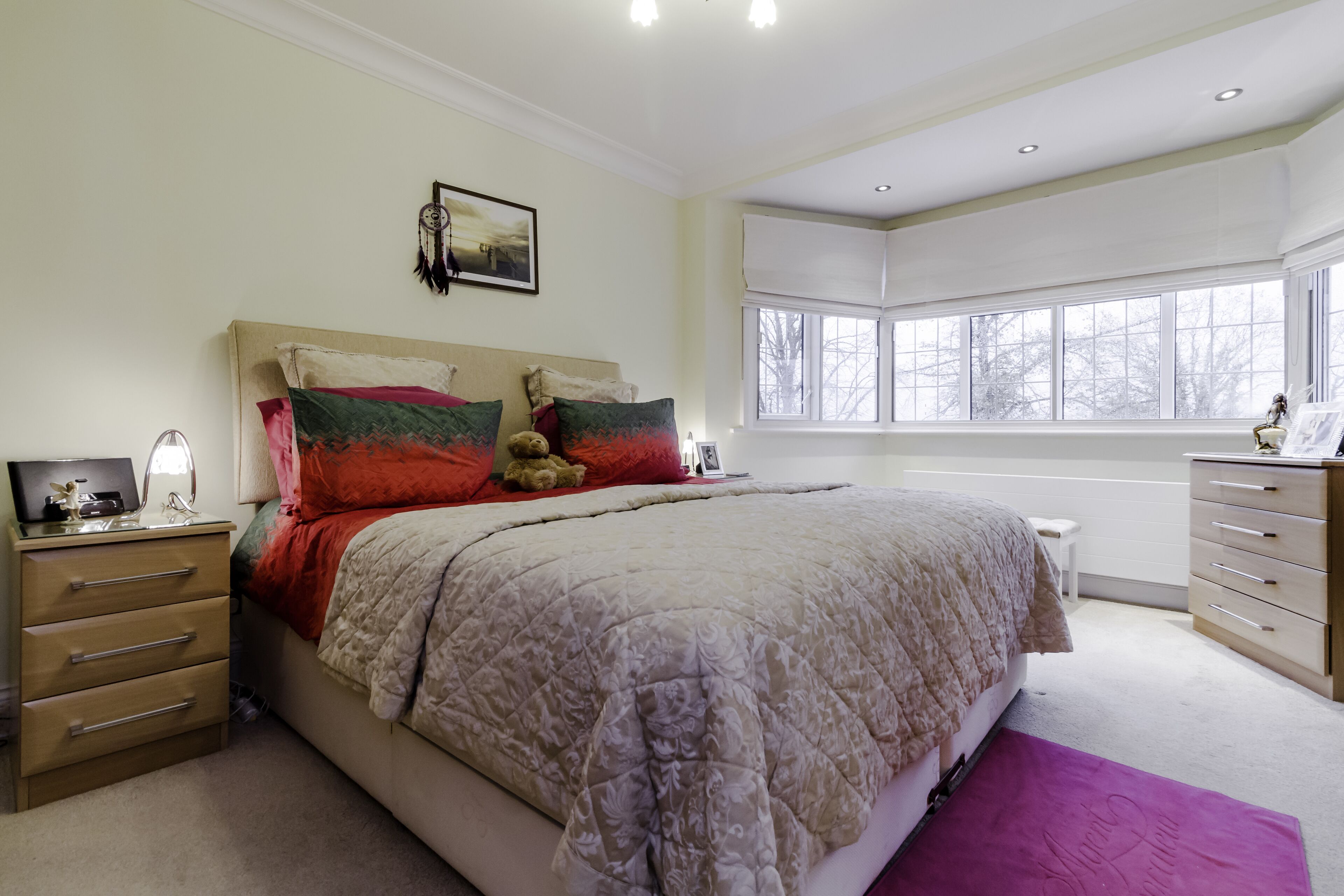 A bedroom with a large bed, a nightstand, a dresser, and a window with a view of trees.