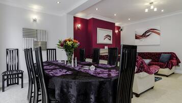 A dining area with a table set for four, surrounded by black chairs, a sofa, and a red accent wall.