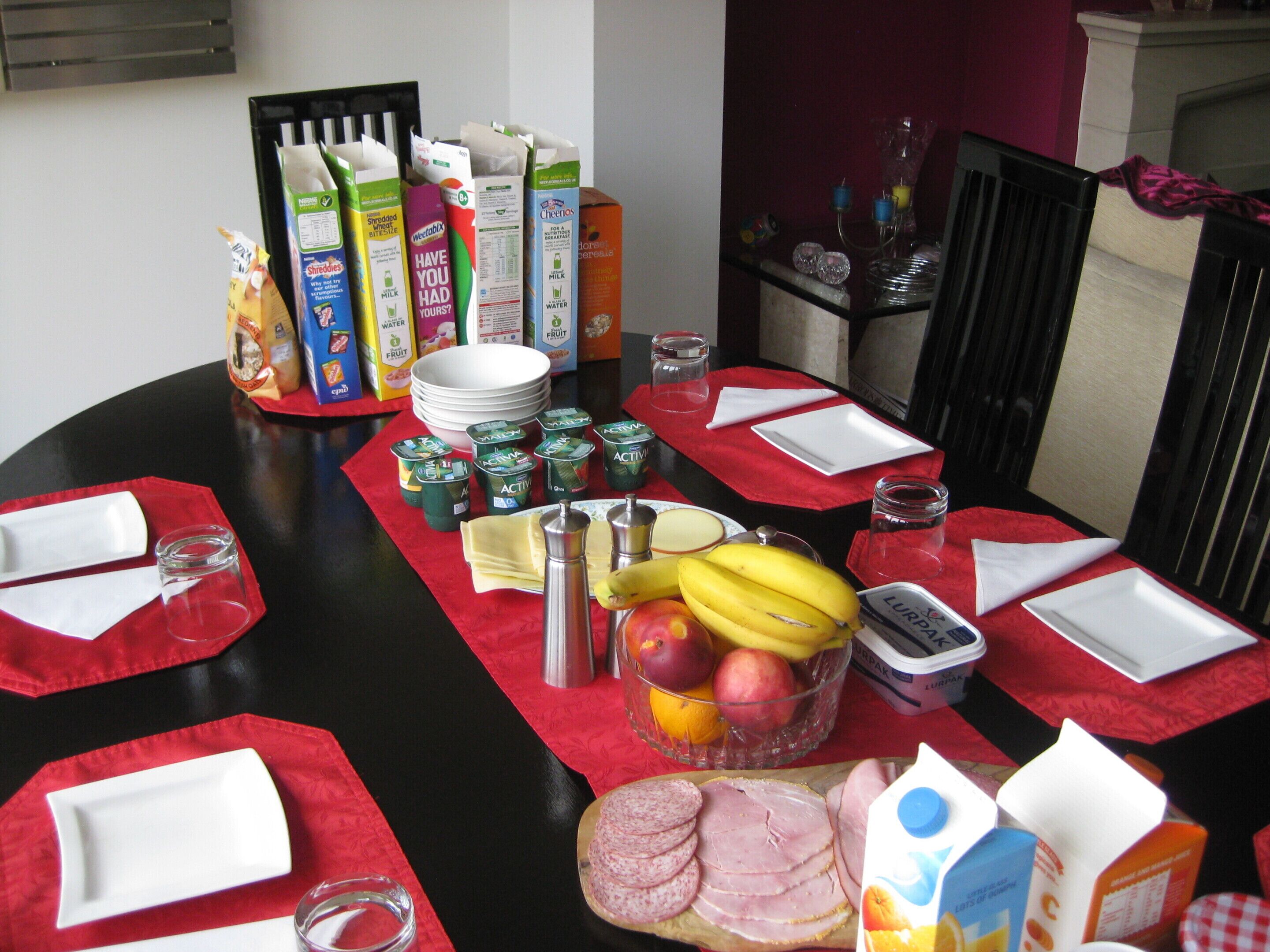 A breakfast table set with various food items, including fruits, dairy products, and condiments.