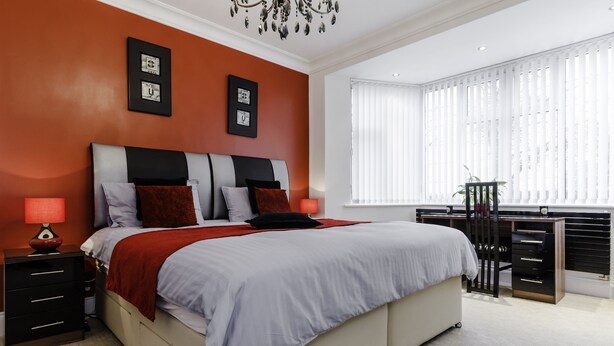 Een moderne slaapkamer met een groot bed, twee nachtkastjes, een kast en een raam met jaloezieën.