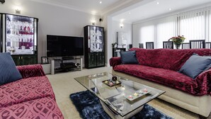 Een moderne woonkamer met een glazen salontafel, rode gestreepte banken, een flatscreen televisie en een kast met glazen deuren.