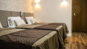 A hotel room with two beds, each with a quilted bedspread, a headboard, and two wall-mounted lights.