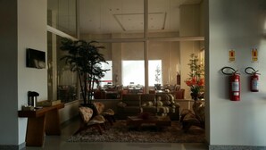 A spacious living area with a large window, comfortable seating, a fire extinguisher, and a plant. - Hotel Caju de Ouro (Feira de Santana)