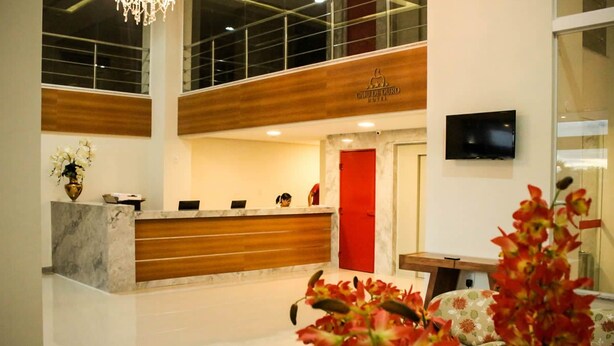 A hotel reception area with a marble counter, a red door, and a television mounted on the wall. - Hotel Caju de Ouro (Feira de Santana)