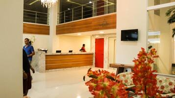 Zona de recepción de un hotel con un mostrador de mármol, una puerta roja y un televisor en la pared.