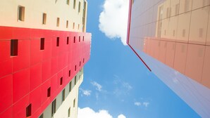 A modern building with a red and white facade, large windows, and a clear sky with clouds. - Lagoa Flat Hotel (Lagoa da Prata)
