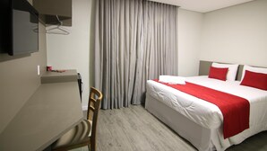 A hotel room with a bed, a desk, a chair, a TV mounted on the wall, and a window with curtains. - Lagoa Flat Hotel (Lagoa da Prata)