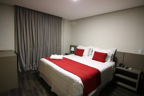 A hotel room with a large bed, red and white bedding, a bedside table with a lamp, and a curtain on the window. - Lagoa Flat Hotel (Lagoa da Prata)