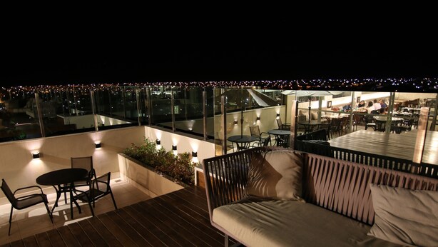 A rooftop terrace with a wooden deck, a sofa, and a dining area with tables and chairs. - Lagoa Flat Hotel (Lagoa da Prata)