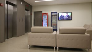 A lobby with two elevators, a Coca-Cola refrigerator, a Pepsi refrigerator, and a television displaying two men in suits. - Lagoa Flat Hotel (Lagoa da Prata)