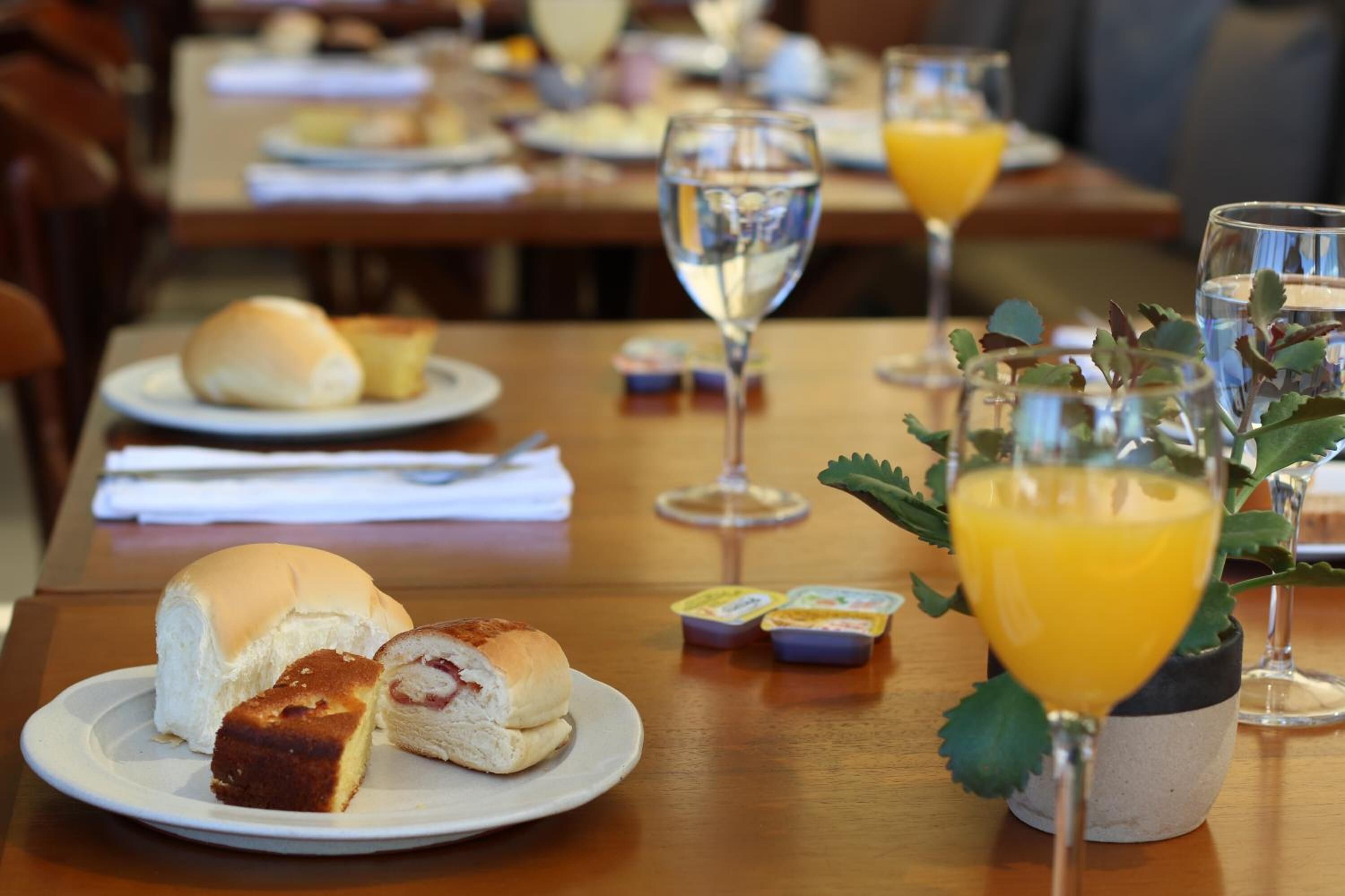 A dining table with plates of food, including buns and a slice of cake, and glasses of water and orange juice.