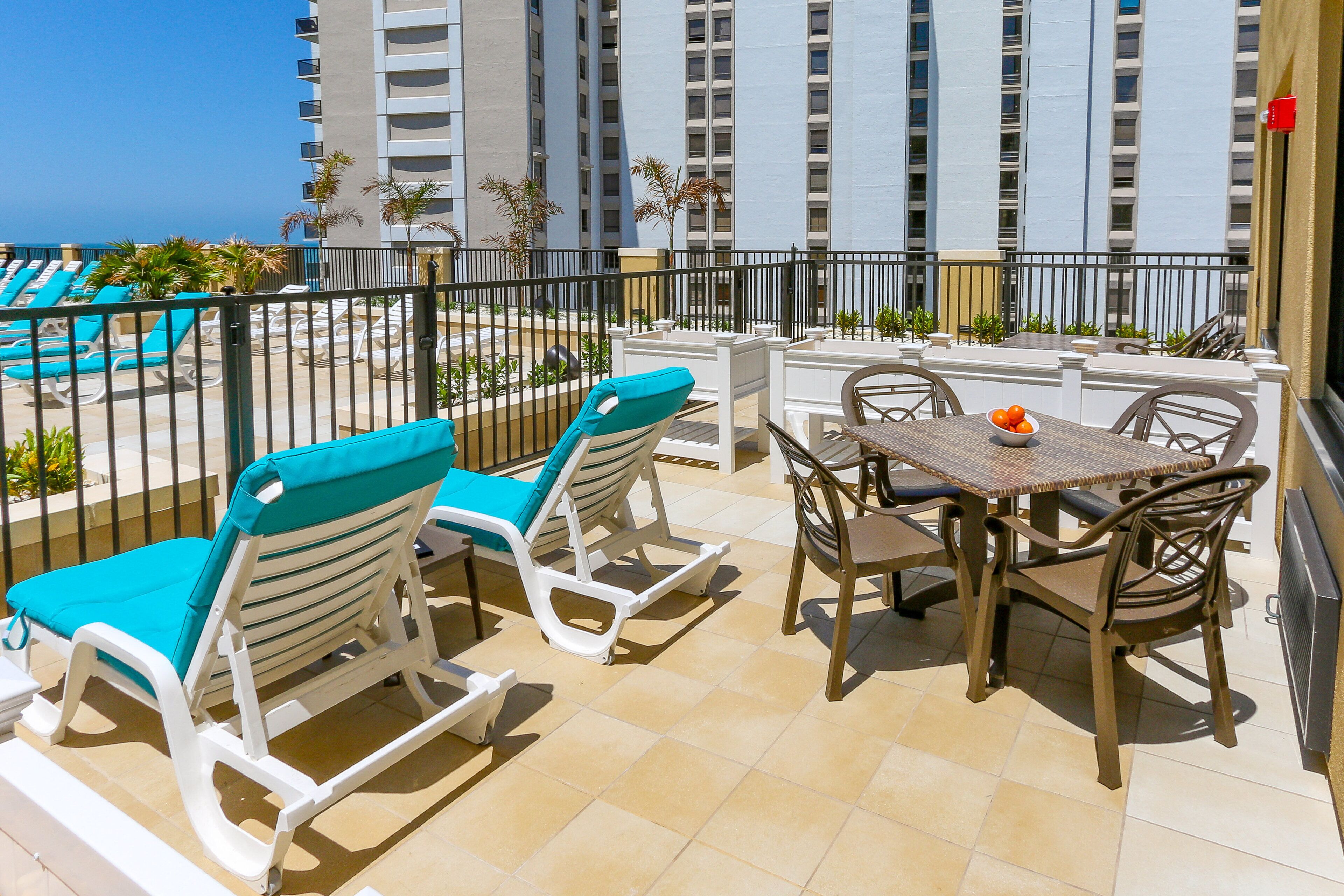 Ein Balkon mit Liegestühlen und einem Tisch, mit Blick auf einen Pool und Hochhäuser.