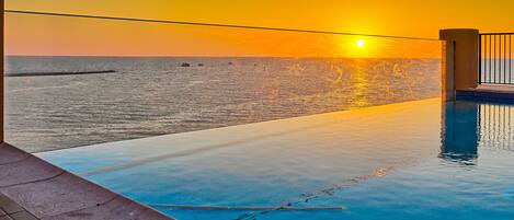 A swimming pool with a view of the ocean during sunset.