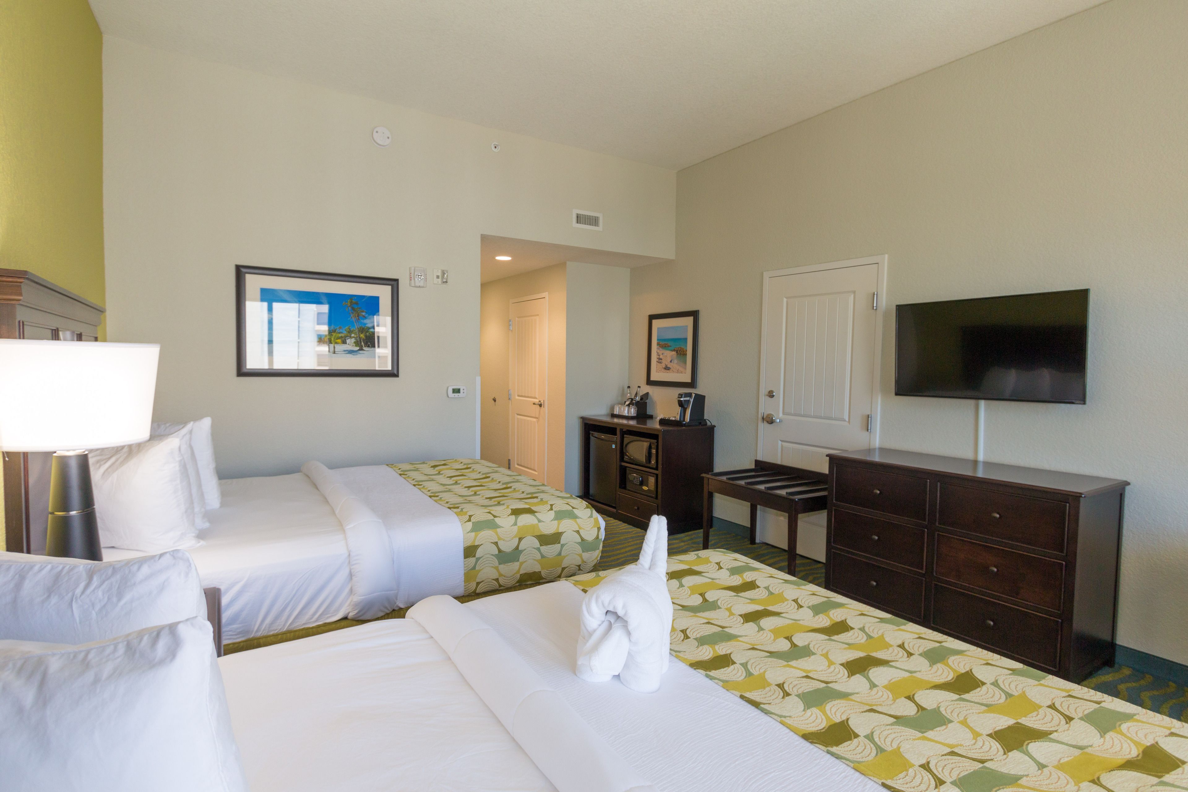 A hotel room with two beds, a TV, a dresser, and a door leading to another room.