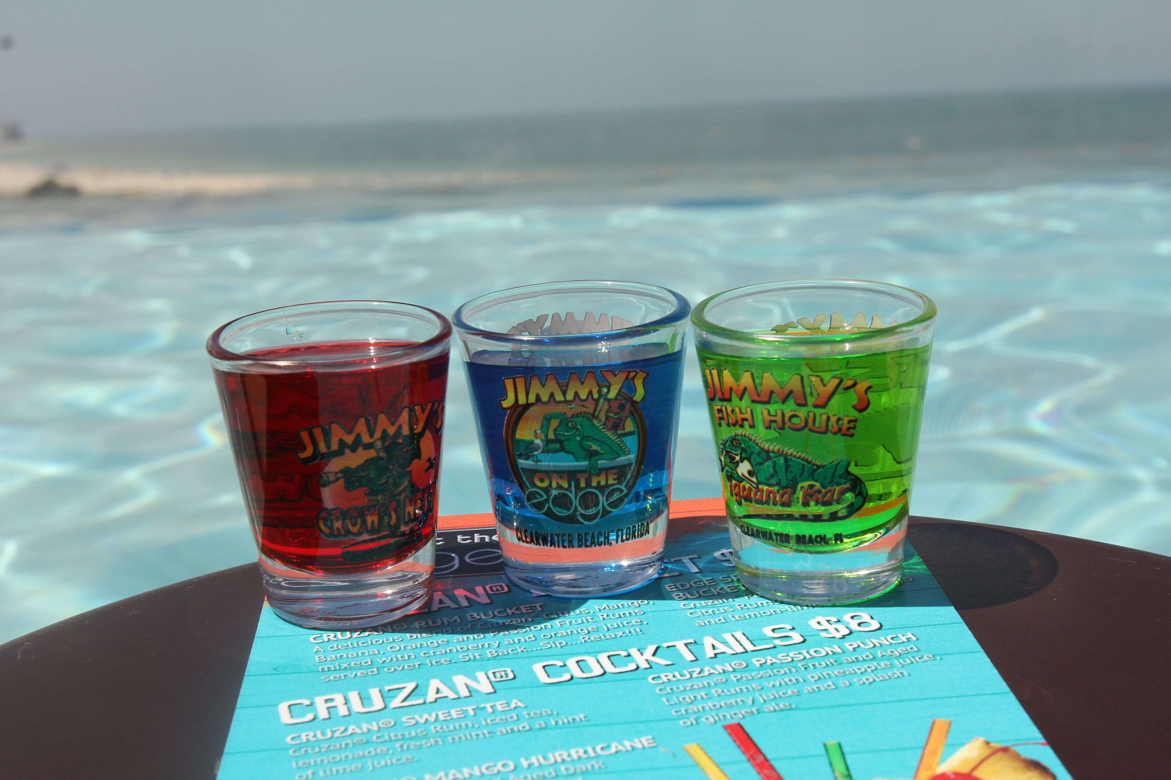Three Jimmy John's branded shot glasses on a menu board.