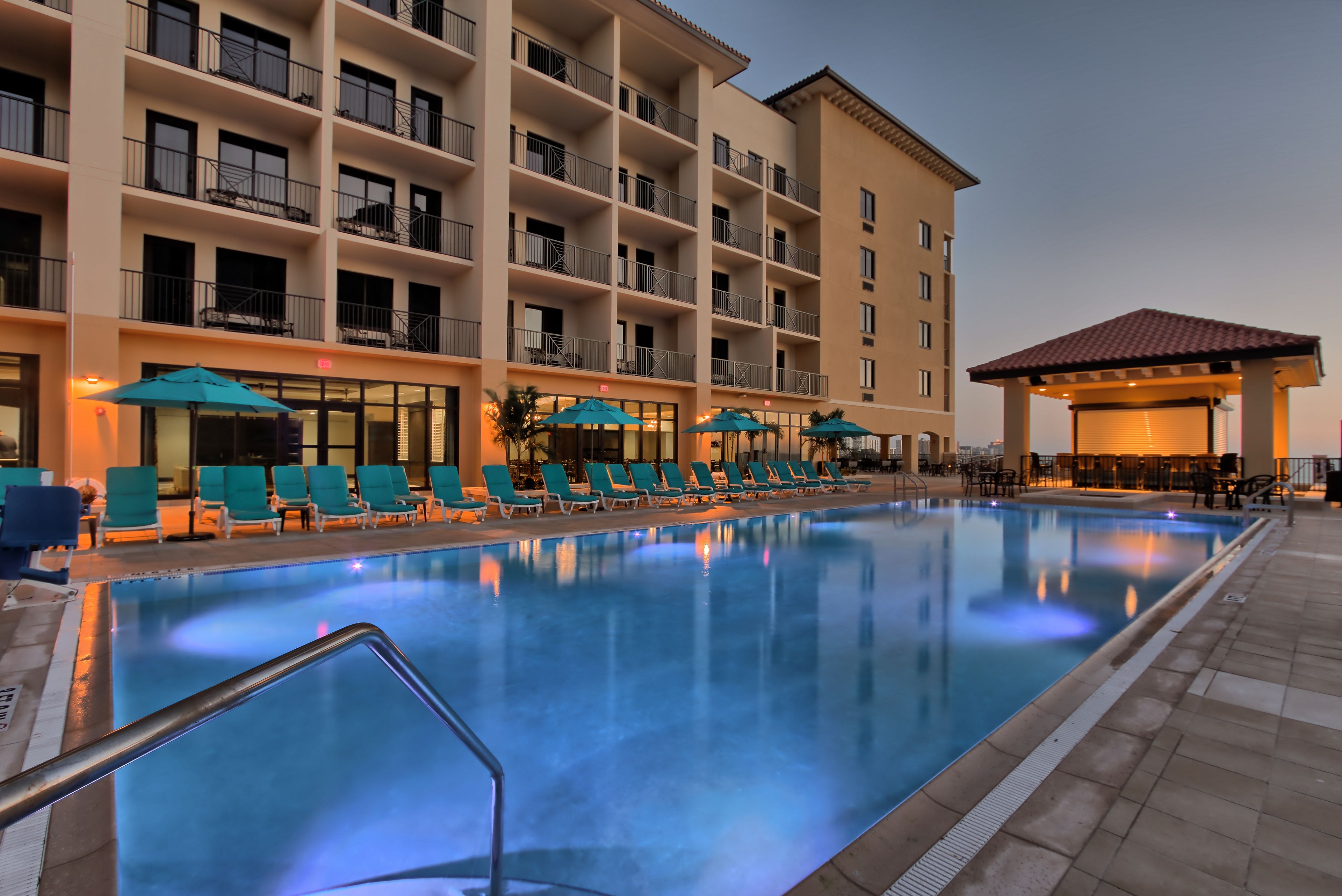 A hotel pool area with a large pool, lounge chairs, and a building with multiple balconies.