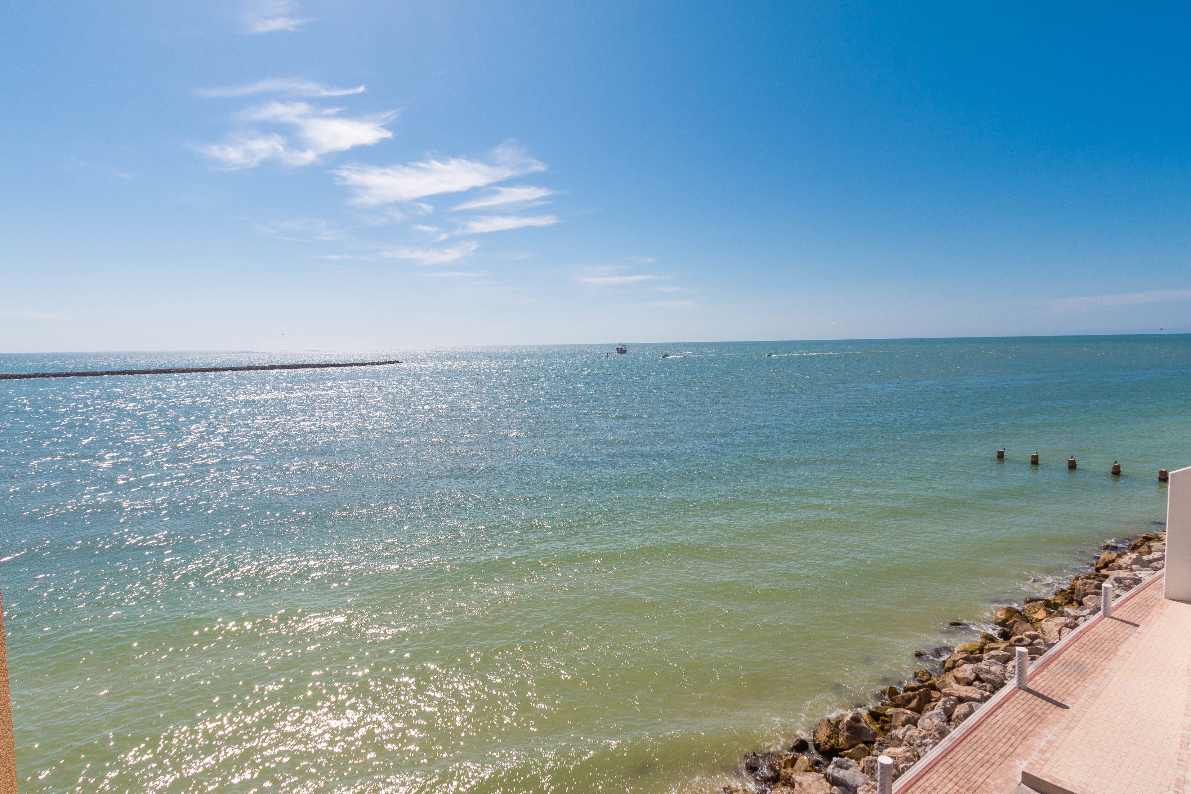 A coastal view with a clear sky, calm sea, and a rocky shoreline.