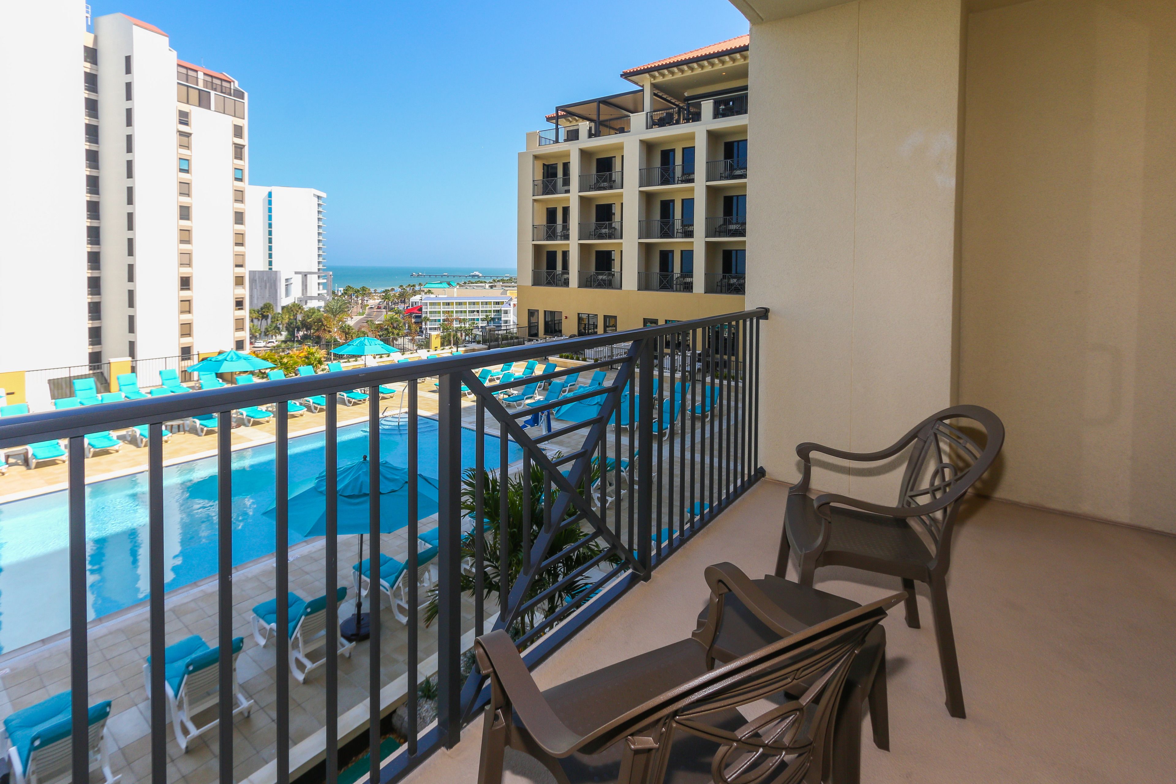 A balcony with a view of a pool and ocean, featuring a table and chairs.