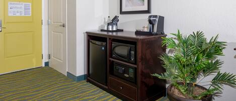 A hotel room with a yellow door, a minibar, a microwave, a coffee maker, and a potted plant.