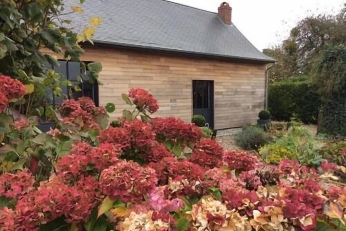 A wooden house with a grey roof, surrounded by a garden with hydrangea bushes.