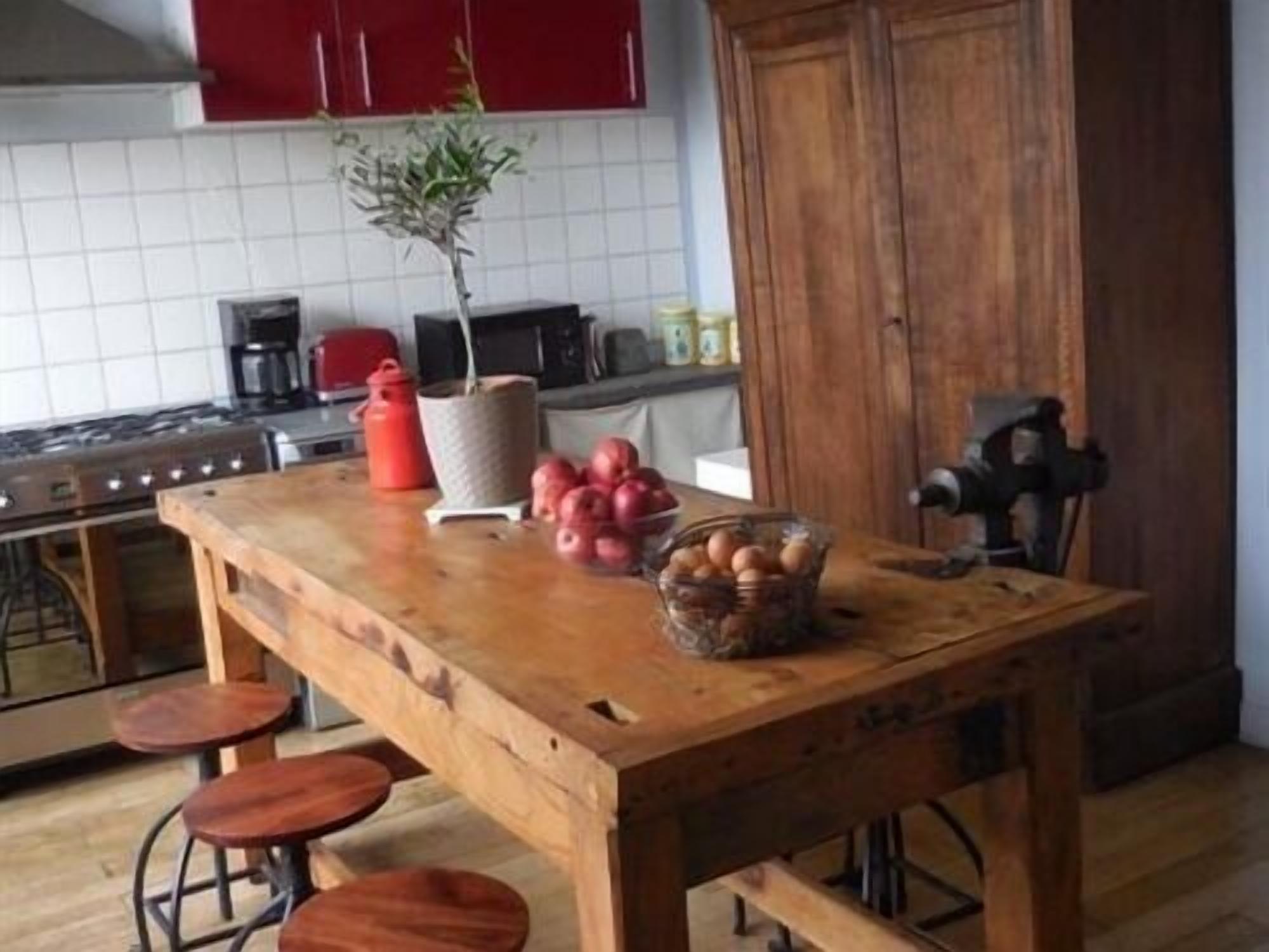 A kitchen with a wooden table, red cabinets, a gas stove, and a coffee maker.