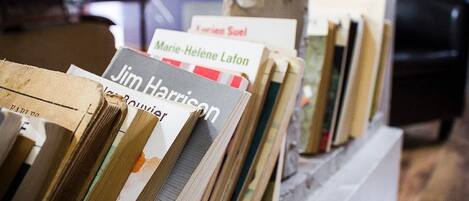 Una hilera de libros en un estante, en una habitación con un pilar de concreto y una silla negra al fondo.