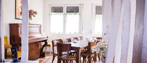 A dining area with a wooden table and chairs, a piano, and a window with blinds.