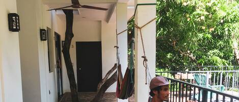 A man sitting on a stone staircase in a covered area with a hammock and a ceiling fan.